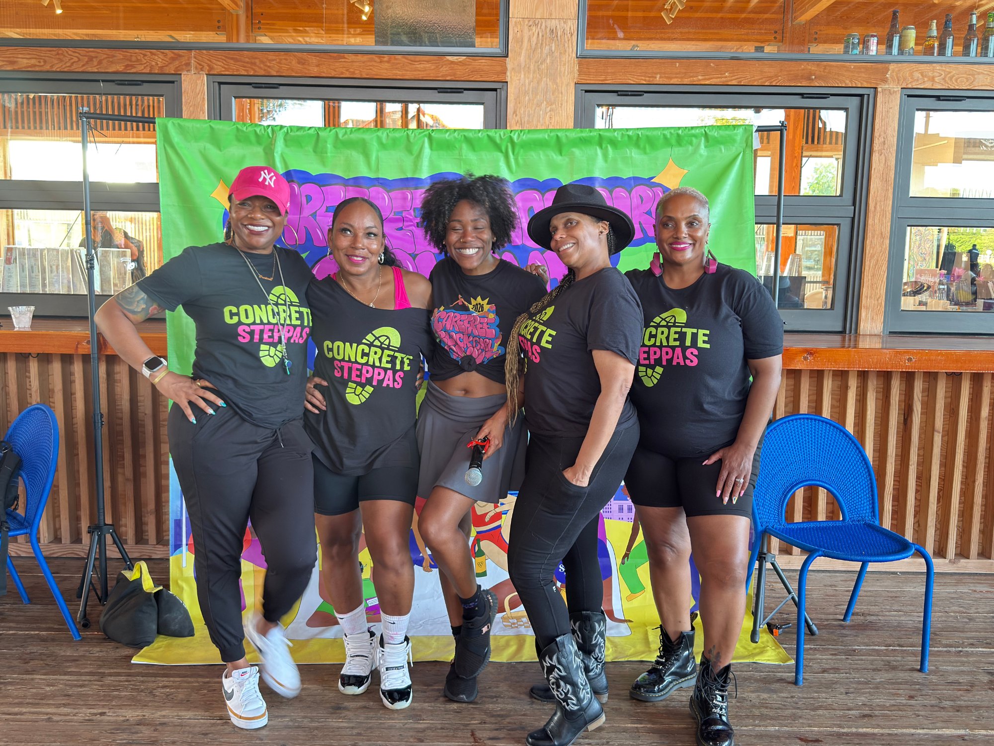 Five people pose together indoors, wearing black Concrete Steppas™ shirts with pink and green lettering.
